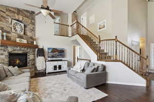 Living area featuring a high ceiling, dark wood finished floors, ceiling fan, stairs, and a stone fireplace
