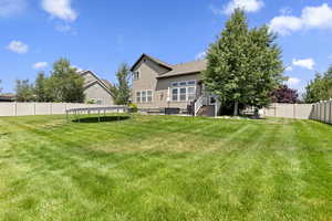 Rear view of house featuring a trampoline, a fenced backyard, and stucco siding