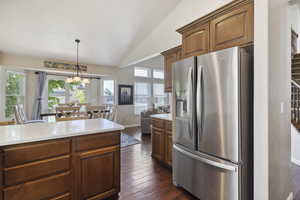 Kitchen featuring stainless steel refrigerator with ice dispenser, vaulted ceiling, light countertops, pendant lighting, and dark wood-style flooring