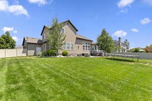 Rear view of property featuring a trampoline, a fenced backyard, and stucco siding