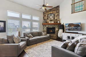 Living area with a ceiling fan, dark wood finished floors, high vaulted ceiling, and a fireplace