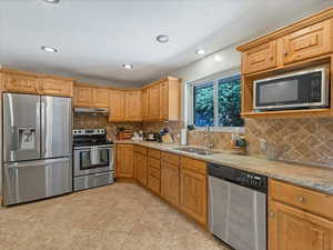 Kitchen featuring appliances with stainless steel finishes, under cabinet range hood, light stone countertops, tasteful backsplash, and recessed lighting
