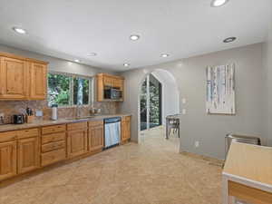 Kitchen featuring dishwasher, arched walkways, healthy amount of natural light, backsplash, and recessed lighting