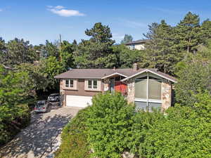 View of front of property featuring stone siding, driveway, an attached garage, and a chimney