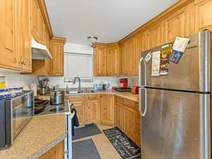 Kitchen featuring freestanding refrigerator, under cabinet range hood, light countertops, and white range with electric stovetop