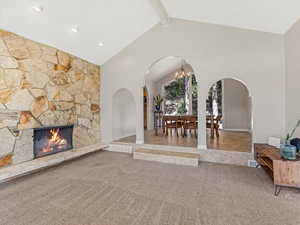 Living area featuring arched walkways, carpet floors, a fireplace, beam ceiling, and high vaulted ceiling