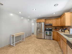 Kitchen with stainless steel appliances, under cabinet range hood, decorative backsplash, recessed lighting, and light stone counters