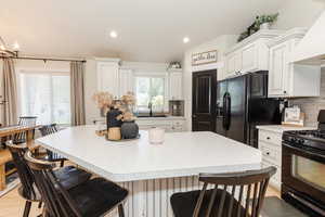 Kitchen featuring black appliances, a kitchen breakfast bar, backsplash, custom range hood, and recessed lighting
