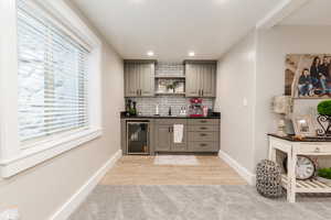 Indoor wet bar with beverage cooler, backsplash, recessed lighting, and light wood finished floors