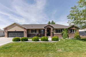 Single story home with brick siding, an attached garage, a front yard, driveway, and roof with shingles