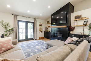Living room featuring wood finished floors, vaulted ceiling, a large fireplace, recessed lighting, and french doors