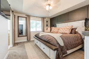 Bedroom featuring a raised ceiling, light carpet, a barn door, and ceiling fan