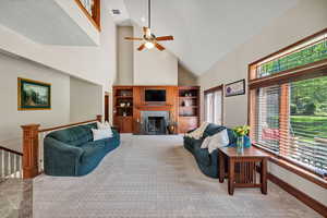 Carpeted living room featuring high vaulted ceiling, a ceiling fan, and a fireplace