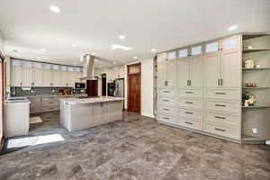 Kitchen with island exhaust hood, appliances with stainless steel finishes, open shelves, a center island, and recessed lighting
