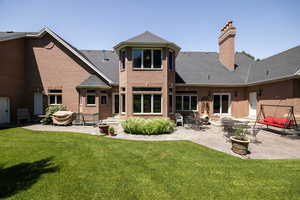 Back of house featuring a chimney, brick siding, a yard, and a patio