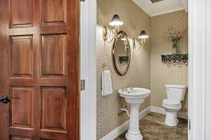 Half bath featuring ornamental molding and wallpapered walls