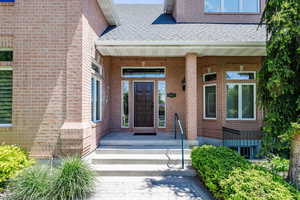 Doorway to property featuring roof with shingles and brick siding