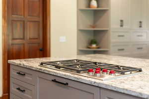 Kitchen with stainless steel gas stovetop, light stone countertops, open shelves, and gray cabinets