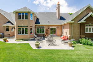 Rear view of house featuring a chimney, brick siding, a yard, and a patio area