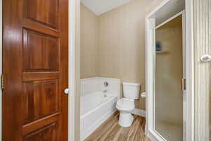 Bathroom with wallpapered walls, wood finished floors, a bath, and a shower stall