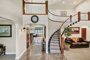 Entrance foyer featuring arched walkways, a towering ceiling, stairway, marble tiled floors, and recessed lighting