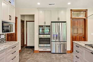 Kitchen with stainless steel appliances, marble finish flooring, light stone countertops, white cabinets, and recessed lighting