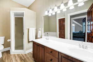 Ensuite bathroom featuring wallpapered walls, wood finished floors, double vanity, a garden tub, and a shower stall