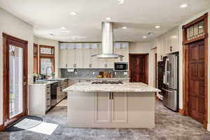 Kitchen featuring freestanding refrigerator, island exhaust hood, dishwashing machine, black microwave, and gas cooktop