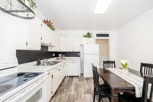 Kitchen with white appliances, light countertops, white cabinetry, decorative backsplash, and light wood-style flooring
