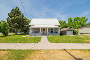 View of front of property with covered porch, a garage, a front lawn, a metal roof, and driveway