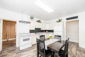 Kitchen featuring white appliances, light countertops, decorative backsplash, and white cabinetry
