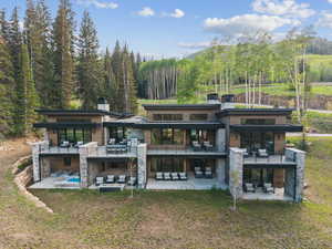 Back of property with a patio area, stone siding, a view of trees, and a balcony
