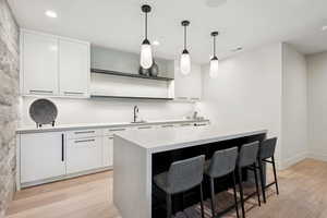 Kitchen with light wood-style floors, light countertops, white cabinets, a breakfast bar area, and recessed lighting