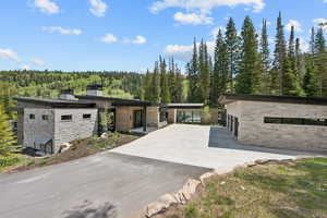 View of front of home with stone siding, a forest view, and concrete driveway
