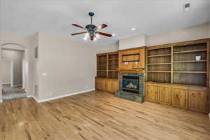 Unfurnished living room with arched walkways, light wood-style floors, a ceiling fan, a tile fireplace, and recessed lighting