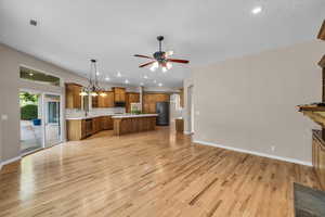 Kitchen with stainless steel appliances, brown cabinetry, open floor plan, light countertops, and light wood finished floors