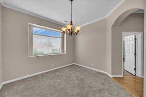 Spare room with crown molding, arched walkways, a chandelier, and carpet flooring