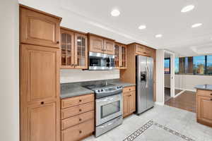 Kitchen with appliances with stainless steel finishes, glass insert cabinets, dark stone counters, recessed lighting, and light tile patterned floors