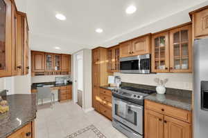 Kitchen featuring glass insert cabinets, appliances with stainless steel finishes, built in study area, brown cabinetry, and recessed lighting
