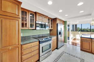 Kitchen with appliances with stainless steel finishes, recessed lighting, glass insert cabinets, and brown cabinets
