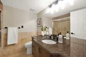 Full bathroom featuring vanity, tile walls, a wainscoted wall, tiled shower, and light tile patterned floors