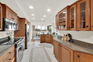 Kitchen featuring glass insert cabinets, inlaid floor details, appliances with stainless steel finishes, recessed lighting, and brown cabinetry