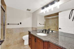Full bath featuring tile walls, vanity, a shower stall, a wainscoted wall, and light tile patterned floors