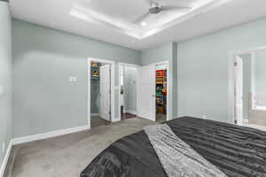 Carpeted bedroom featuring a walk in closet, a closet, a tray ceiling, recessed lighting, and ensuite bathroom