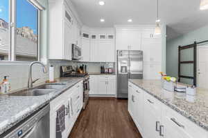 Kitchen with appliances with stainless steel finishes, a barn door, dark wood-style floors, decorative backsplash, and white cabinetry