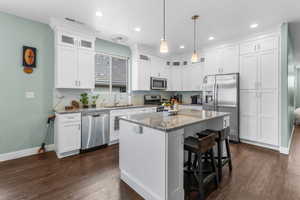 Kitchen featuring appliances with stainless steel finishes, white cabinetry, dark wood finished floors, a breakfast bar, and recessed lighting