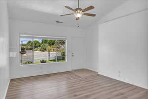 Empty room featuring wood finished floors, a ceiling fan, and lofted ceiling
