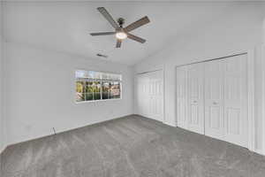 Unfurnished bedroom featuring two closets, carpet flooring, lofted ceiling, and ceiling fan