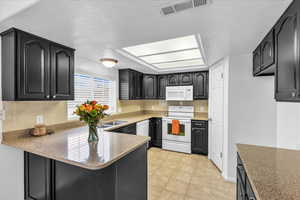 Kitchen with white appliances, tasteful backsplash, a peninsula, a textured ceiling, and light countertops