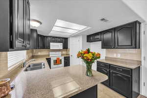 Kitchen featuring white appliances, dark cabinetry, backsplash, and a peninsula
